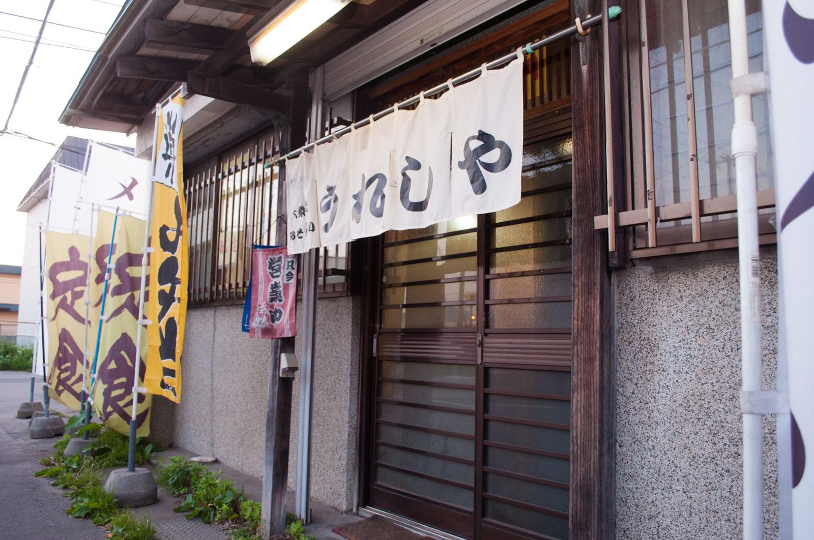 店の外観を斜めから。暖簾と黄色い「定食」ののぼり