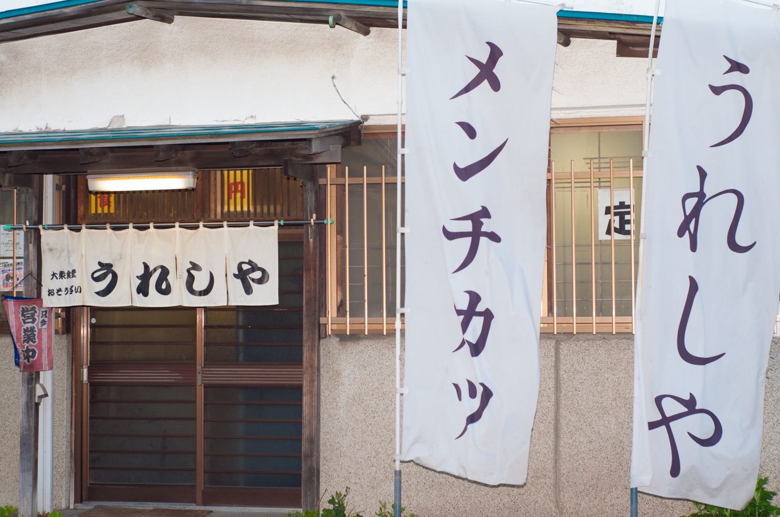 店の入口。「うれしや」の暖簾と、「メンチカツ」「うれしや」ののぼり