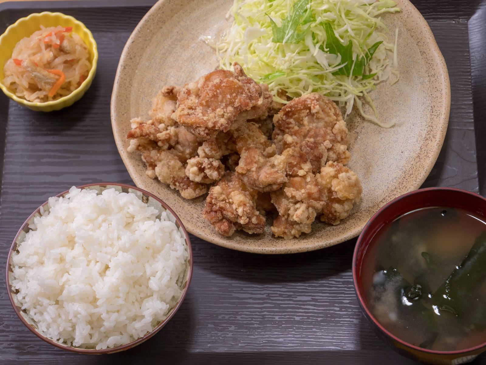うま塩からあげ定食の全景。黒いお盆にご飯、味噌汁、小鉢、からあげとキャベツの皿