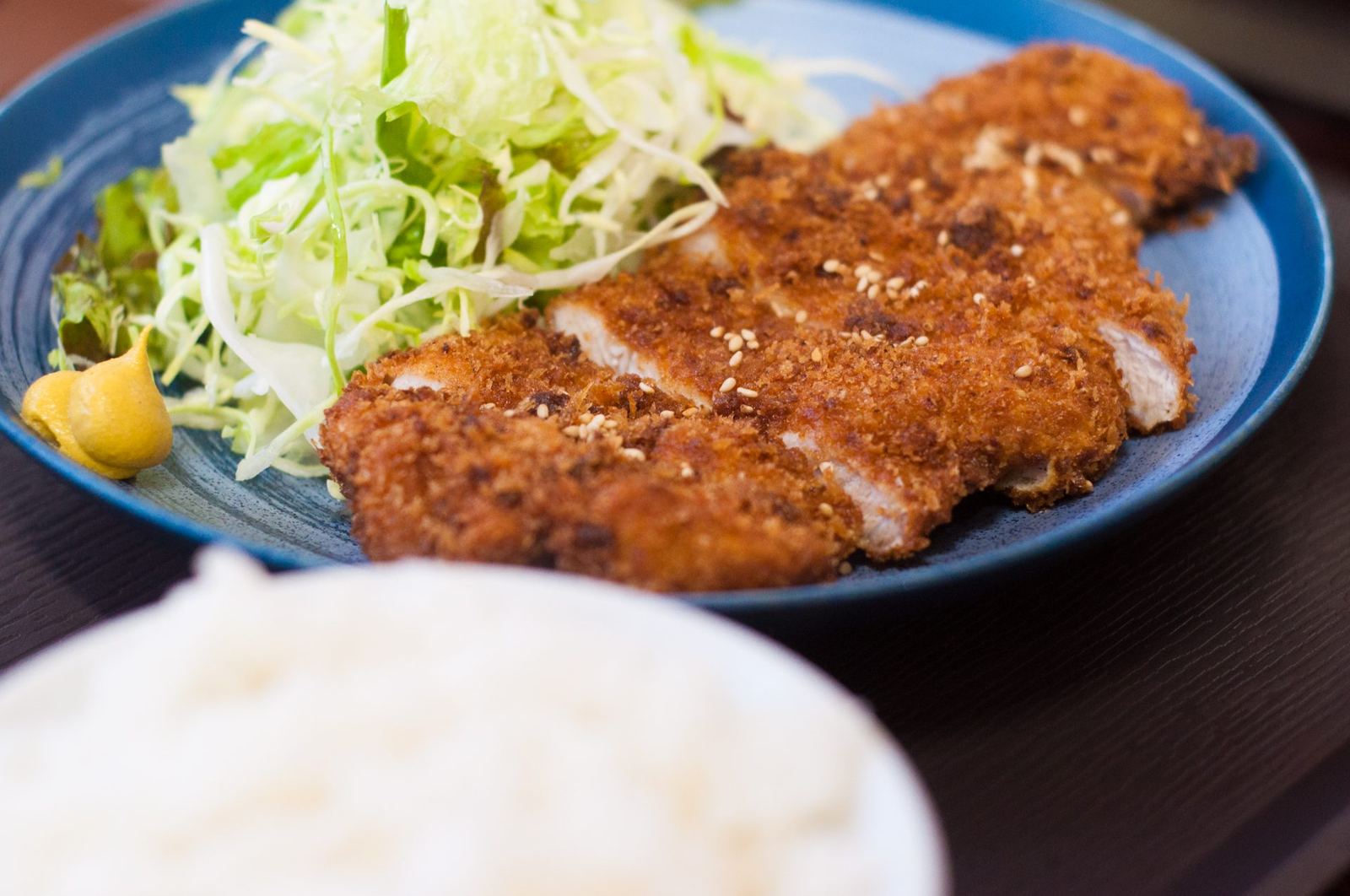 青い皿のロースカツ。千切りキャベツと辛子、手前にご飯